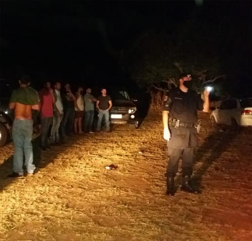 Policial, de lanterna em mãos, identifica os participantes da festa